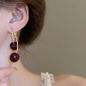 Close-up of deep red resin cherry drop earrings worn on ear with gold metal stems