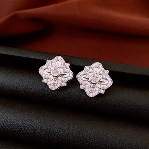 Macro shot of silver floral stud earrings with full zircon inlay on a dark leather background