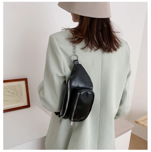 Detail of stylish black faux leather crossbody bag with silver chain strap worn by model