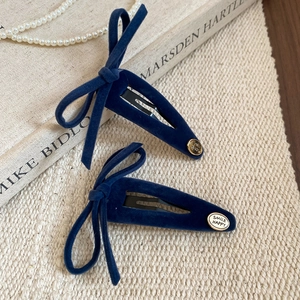 Detail of navy blue flocked bow hair clips with gold smile charms on knit background