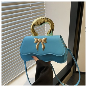 Detail of blue handbag featuring a scalloped edge and golden bow-shaped metal buckle