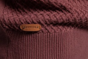 Macro detail of knit cable patterns and a brand leather patch on a cotton sweater