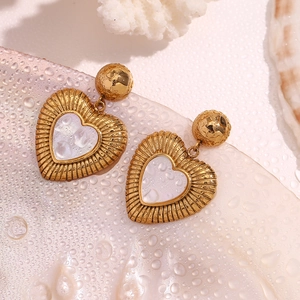 Détail de boucles d'oreilles cœur en or avec nacre sur fond de coquillage et corail