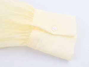 Détail du poignet d'une chemise en mousseline jaune clair avec plis et bouton rond blanc
