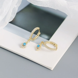 Macro shot of gold hoop earrings with white zircon accents and blue opal diamond pendant