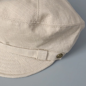 Détail de la casquette gavroche en lin beige montrant la texture et le bouton bronze