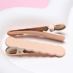 Close-up of two wave-shaped hair clips in cream pink with a smooth lacquered finish