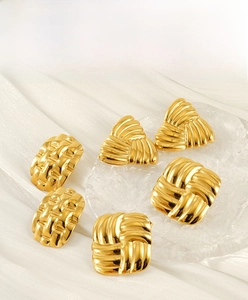 Detailed view of geometric gold earrings with textured stripes on white silk fabric