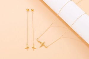 Detailed view of golden heartbeat necklace and long drop earrings on peach background