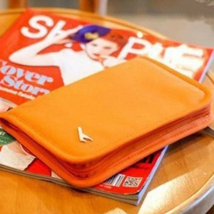 Orange multipurpose travel passport wallet with metal bird logo on a red magazine background