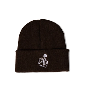 Détail d'un bonnet en tricot marron foncé avec broderie d'un squelette buvant du thé