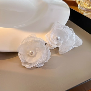 Detail of elegant white tulle camellia earrings with pearl center on ceramic dish