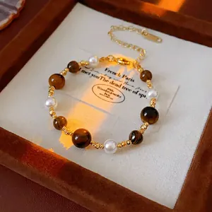 Gold-plated geometric beaded bracelet with tiger eye stone and pearls on a velvet tray