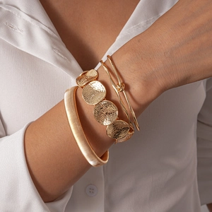 Detailed view of three gold metallic bracelets featuring woven textures and hammered discs