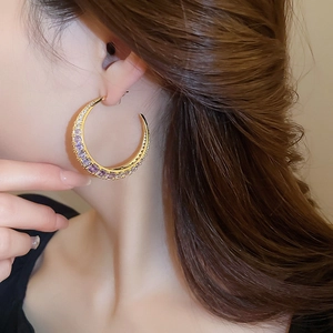 Detail of a large gold C-shaped earring with purple and white zircon stones on a model