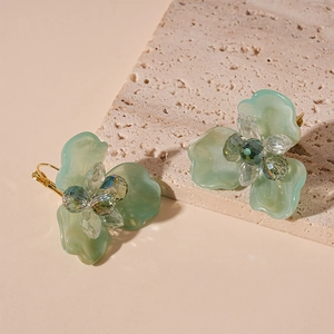 Detailed close-up of light green resin flower earrings with crystal accents and gold clasp