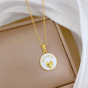 Detail of a gold mama necklace with white enamel pendant on a soft beige jewelry box