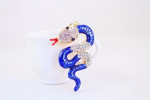 Detailed view of the blue enamel and crystal snake charm hanging on a white ceramic cup