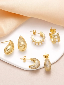 Detailed view of three pairs of gold-plated teardrop and pearl studded earrings on silk