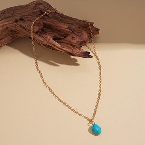 Detail of blue turquoise pendant on gold chain necklace draped over rustic wood