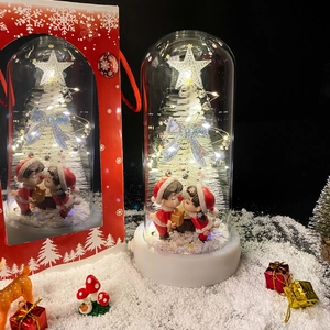 Close-up of lighted Christmas glass dome with snow trees and miniature couple in red box