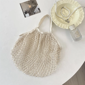 Flat lay of cream woven mesh tote bag with French lifestyle accessories on white surface