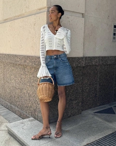 Detail of white crochet knit cardigan featuring V-neck buttons and flared bell sleeves
