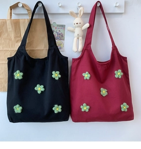 Close-up of canvas tote bags in black and burgundy with green plush flower details
