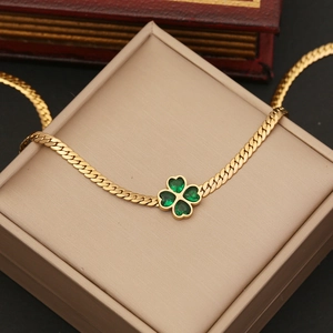 Golden clover pendant necklace with green gemstone on beige jewelry box