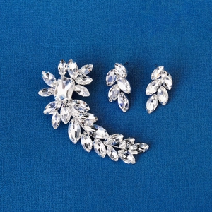 Detailed view of crystal leaf hair clip and matching earrings on blue textured fabric