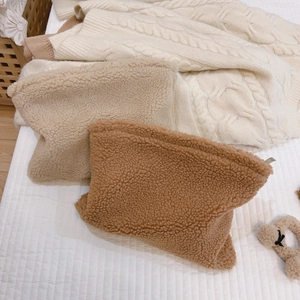 Fuzzy faux fur makeup bag set with scrunchie on cozy quilted white bedding background