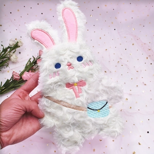 Gros plan d'une trousse lapin en peluche blanche avec broderies et nœud rose décoratif
