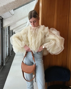 Détail du chemisier en organza beige à volants avec un sac à main demi-lune en cuir