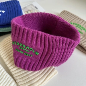 Nahaufnahme von grob gerippten Strickstirnbändern mit bunt besticktem Schriftzug in vielen Farben
