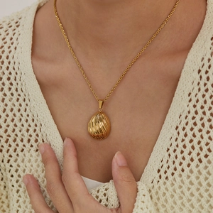 Detail of gold oval shell texture pendant on a twisted rope chain necklace worn by model