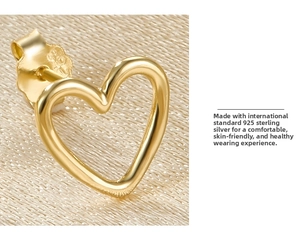 Detailed close-up of hollow heart S925 sterling silver gold stud earrings on silk background