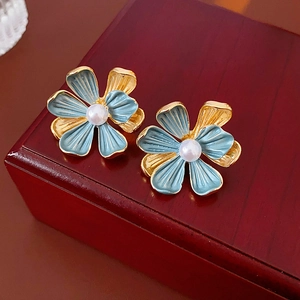 Gros plan de boucles d'oreilles fleur émaillée bleue et perle sur boîte bois