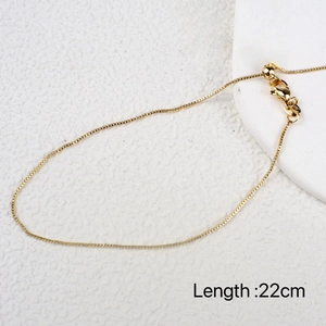 Flat lay of a golden 22cm adjustable chain anklet on a white textured background