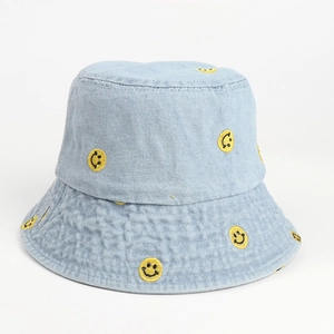 Close-up of yellow smiley face embroidery and texture on light blue denim bucket hat