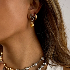 Dettaglio di orecchini a cuore bicolore indossati con una collana di perline abbinata