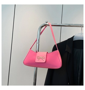 Detailed view of pink faux leather baguette bag with a golden bow buckle on a metal hanger