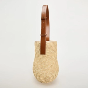 Handwoven straw bucket bag with adjustable brown leather shoulder strap on white background