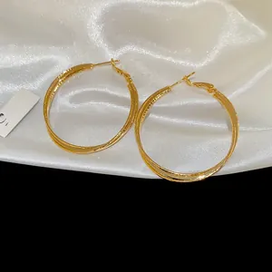 Detailed view of 18k gold plated double layer crossover hoop earrings on white satin silk