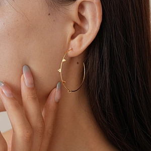 Model wearing large golden geometric hoop earring with pyramid studs in a warm setting