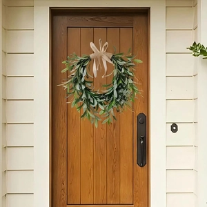 Artificial olive leaf wreath with burlap bow hanging on a dark wood front door decor