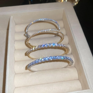 Detailed view of four slim zircon-encrusted open bangles in gold and silver on a beige tray
