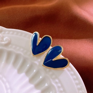 Elegant gold-edged blue heart stud earrings on a white ceramic tray with silk background