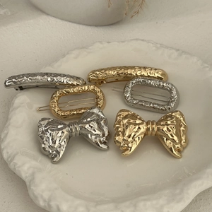 Set of gold and silver hammered metal hair clips with bow and oval shapes in a dish