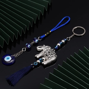 Blue evil eye and silver elephant keychain with tassels on a dark reflective surface