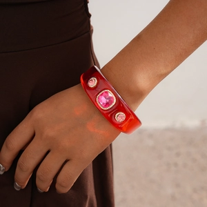 Detail of red translucent resin bangle featuring square pink rhinestones on a model
